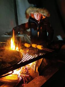 une personne qui cuisine de la nourriture sur un grill à côté d'un feu dans l'établissement Máttaráhkká Northern Light Lodge, à Kiruna