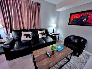 a living room with a black leather couch and a table at Canadian Rockies Chalets by Trilink - 2 & 3 Bedroom Condos - Self Check-In - Walking Distance to Downtown - Free Parking - Pet-Friendly - No AC in Canmore