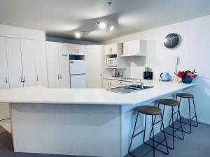 a kitchen with white cabinets and a counter with stools at Oceanside Apartment in Mount Maunganui