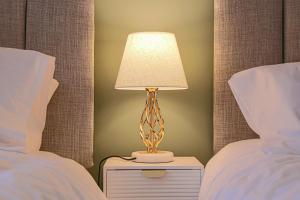a lamp on a night stand next to two beds at Central MK House - Sleeps Up To 9 Guests - Free Parking, Fast Wifi, Pool Table and Smart TV with Sky TV and Netflix by Yoko Property in Milton Keynes