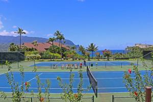 dos pistas de tenis con palmeras y el océano en el fondo en Hanalei Bay Resort 2302 en Princeville