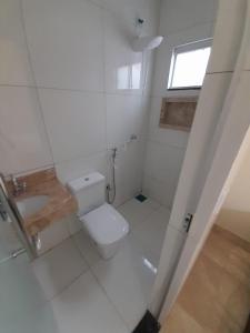 a white bathroom with a toilet and a window at CASA ARUANÃ 5 SUITES in Aruanã