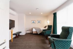 a hotel room with a bed and chairs and a television at Highway Lodge Motel in Balclutha