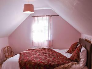 a bedroom with a bed with a red blanket and a window at Arun Cottage in Loxwood