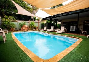 a swimming pool in a yard with chairs and a umbrella at Kimberley Croc Motel in Kununurra