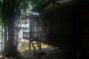 een houten hut met een bank naast een boom bij Pomelo Restaurant and Guesthouse's Fishermen Bungalow & A Tammarine Bungalow River Front in Ban Khon