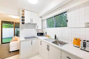a white kitchen with a sink and a microwave at 'Bluey' a Tiny House A-frame Moments to Foreshore in Nightcliff