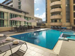 a swimming pool with tables and chairs in a building at Adina Serviced Apartments Canberra James Court in Canberra