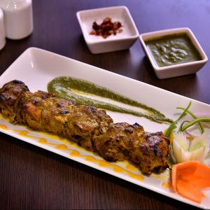 a plate of food with two skewers and a pickle at Brio Hotel in Kolkata