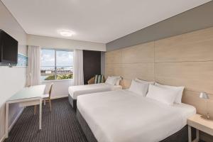 a hotel room with two beds and a desk and a window at Vibe Hotel Darwin Waterfront in Darwin