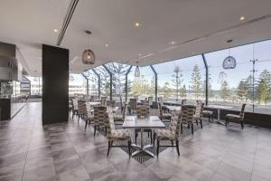 uma sala de jantar com mesas, cadeiras e janelas em Rendezvous Hotel Perth Scarborough em Perth