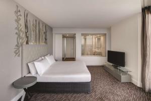 Rendezvous Hotel Perth Scarborough في بيرث: غرفة نوم بسرير ابيض وتلفزيون بشاشة مسطحة