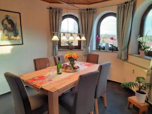 a dining room with a table and chairs and two windows at Haus Am Waldesrand in Fichtelberg