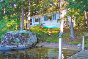 a house in the woods with a rock in the water at Lake Winni Cottage in Moultonborough