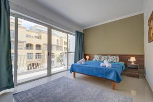 - une chambre avec un lit bleu et une grande fenêtre dans l'établissement Violet Court Apartments and Penthouse in St Julian's By ShortletsMalta, à San Ġiljan