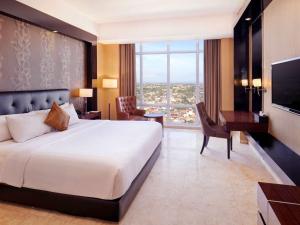 a bedroom with a bed and a desk and a television at Grand Mercure Solo Baru in Solo