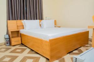 1 dormitorio con cama de madera con sábanas blancas en GIDI LODGE, en Tamale