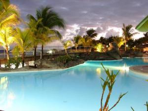a blue pool with palm trees and a bridge at Agréable studio au bord de mer. in Saint-François