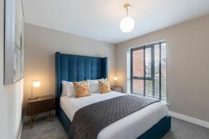 1 dormitorio con 1 cama con cabecero azul y ventana en Elliot Oliver - Luxurious Two Bedroom Apartment With Parking, en Gloucester