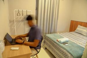 a man sitting at a desk with a laptop in a bedroom at Casa Pequena, Completa e Aconchegante - Tiny House in Palmas