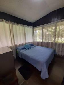 a bedroom with a bed with blue sheets and windows at Hospedaje Finca Agroturistica Doña Rufa in Río Sereno