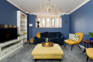 a living room with blue walls and yellow chairs at Cloisters Cottage in Chichester