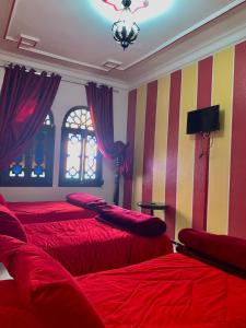 a bedroom with two beds with red sheets and striped walls at Hotel Sevilla in Chefchaouene