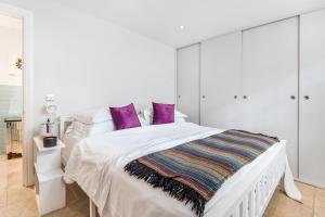 een witte slaapkamer met een wit bed met paarse kussens bij Chepstow Place- Notting Hill in Londen