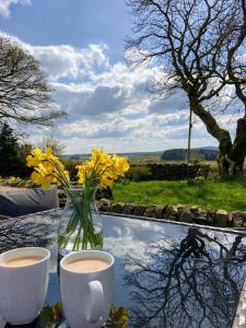 a table with a vase of flowers and two cups of coffee at Glaisters Farmhouse in Castle Douglas