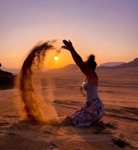 a woman in the desert with the sun in the background at Wadi Rum Meteor camp in Wadi Rum