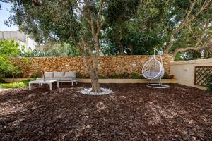 a garden with a tree and a bench and a swing at Bliss Boutique Living in Xagħra