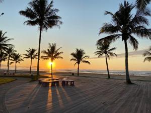 a sunset on a beach with palm trees and benches at Pousada Acqua Infinity PISCINA CLIMATIZADA PÉ NA AREIA in Bertioga