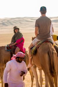 duas pessoas montadas nas costas de um camelo no deserto em Luxury Desert Camp em Al Wāşil