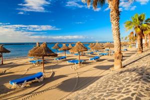 a beach with straw umbrellas and chairs and the ocean at Rosamar 211 Los Cristianos Ocean Views in Arona