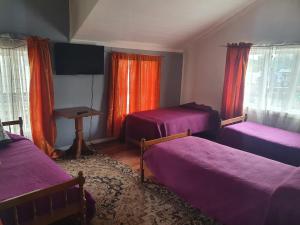 a room with three beds and a table and windows at Hostal Papo in Osorno