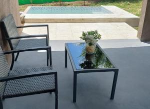 2 Stühle und ein Glastisch mit Blumen auf der Terrasse in der Unterkunft cabañas La Amelia Premium con piscina privada 2 personas in Mina Clavero