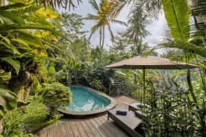 a hot tub in a garden with an umbrella at Mandana Ubud Villa in Ubud