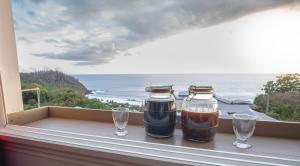 deux bocaux et des verres sur un rebord de fenêtre avec vue sur l'océan dans l'établissement Le Coin d'Azur, à Petite Île