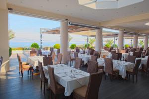 a restaurant with white tables and chairs and the ocean at Kipriotis Panorama Hotel & Suites in Kos