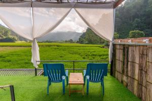 2 sedie e un tavolo su un portico con vista su un campo di เนเจอร์วัลเล่ย์แคมป์ ปางมะผ้า a Pang Mapha