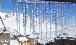 un montón de carámbanos colgando de una ventana con una montaña cubierta de nieve en Duplex Holidays Andorra, en Pas de la Casa