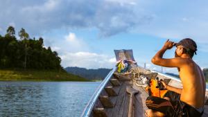 un homme assis sur un bateau sur l'eau dans l'établissement Monkey Mansion - Jungalows & Tours, à Khao Sok