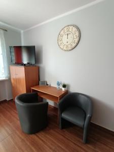 スバジェンツにあるPokoje pod Świerkiemのテーブルと椅子2脚、壁に時計が備わる客室です。