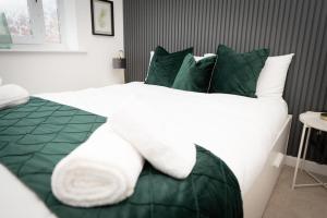 uma cama grande com lençóis e almofadas verdes e brancos em Grand Station Suite em Wolverhampton