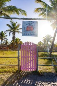 um portão rosa num campo com palmeiras em Pousada Vila Rosa - Caraiva em Caraíva