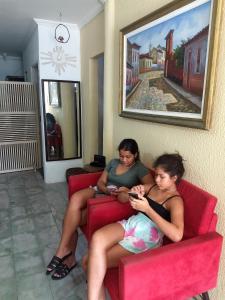 dos mujeres sentadas en un sofá rojo mirando sus celulares en Pousada Aconchego en Aracajú