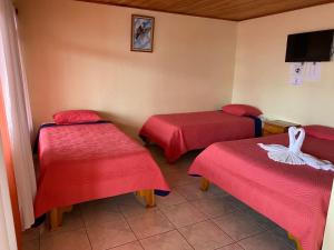 Habitación con 2 camas con sábanas rojas y TV. en Hotel La Puesta Del Sol B&B, en Monteverde