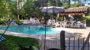 a swimming pool with white chairs and an umbrella at Hotel Chácara das Flores in São Gabriel
