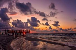 einen Sonnenuntergang über dem Meer mit einem Pier am Strand in der Unterkunft Holiday resort, Sarbinowo in Sarbinowo