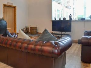 a brown leather couch in a living room with a television at Primrose Cottage - Uk41346 in Cromer